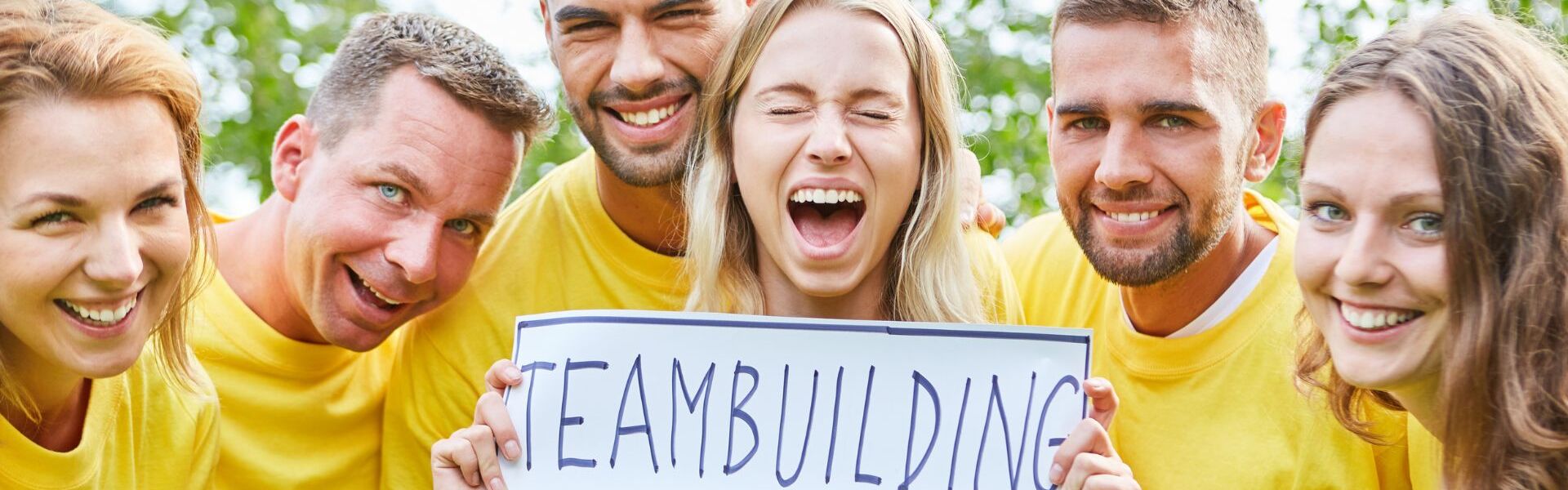 Gruppe von Personen mit gelben Shirts und Schild mit der Aufschrift "Teambuilding"