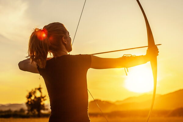 Person mit gespannten Bogen im Sonnenuntergang.
