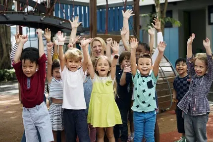 Jubelnde Kinder, die die Arme in die Luft strecken und lachen. Im Hintergrund ein Kinderspielplatz.