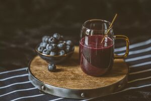 Roter Smoothie im Glas und Blaubeeren auf Tablett.