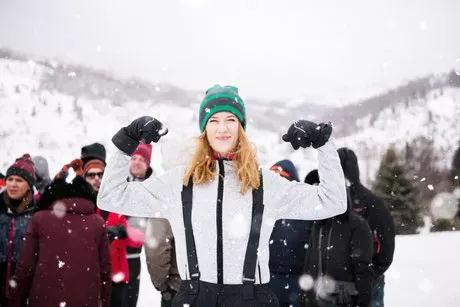 Frau in Winterkleidung im Schnee hält die Arme hoch und freut sich.